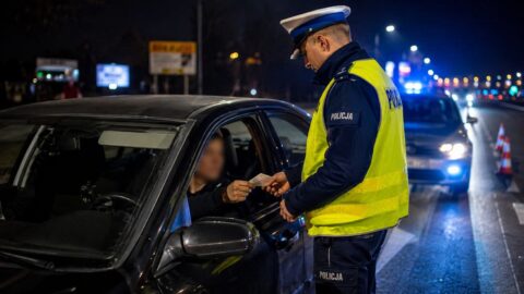 Policjant sprawdza dokumenty kierowcy podczas nocnej kontroli drogowej.